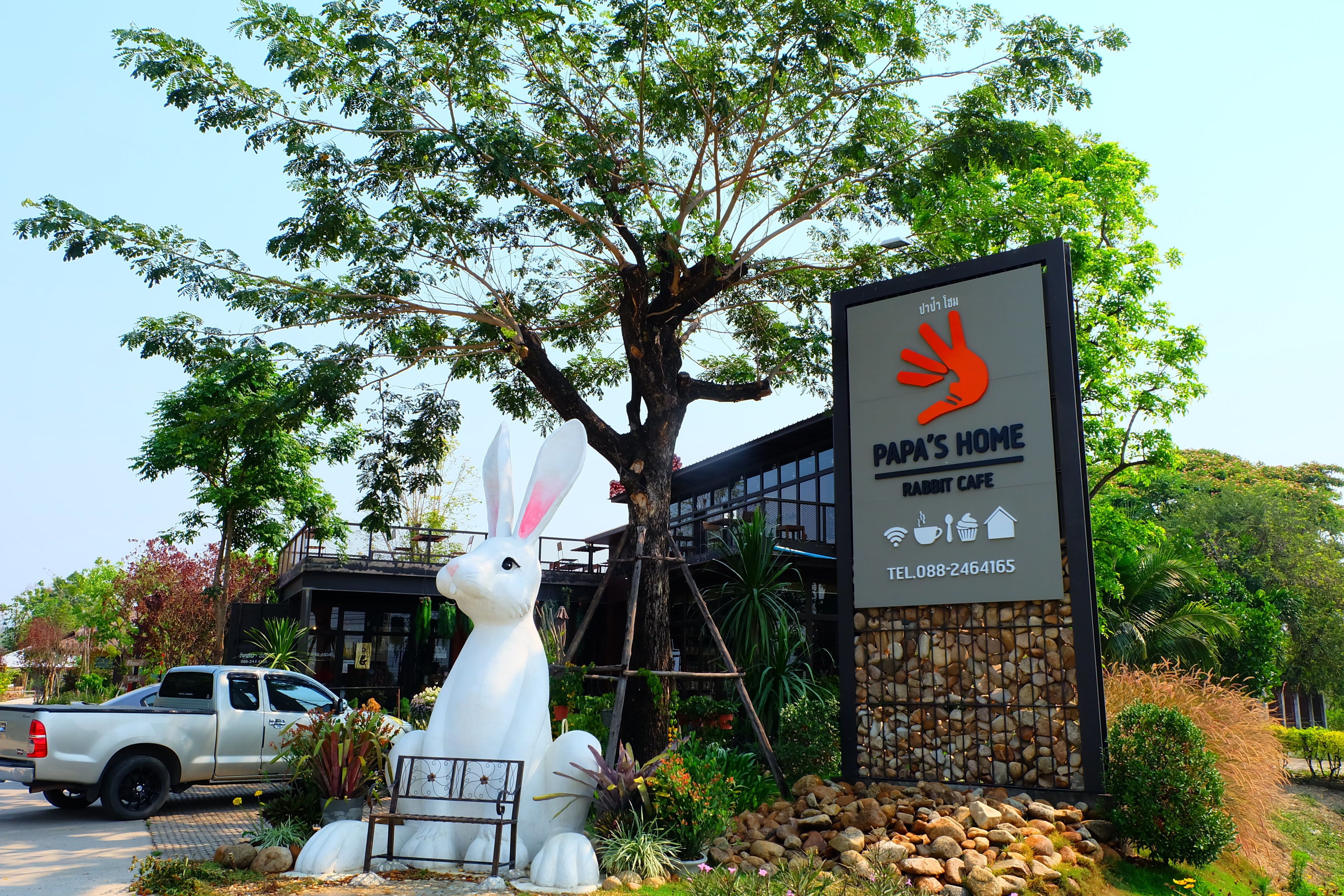 Een groot wit konijnenbeeld voor een gebouw met een bord waarop staat: "Park's Home Rabbit Cafe".