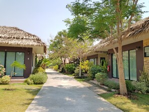 Un sendero conduce a una hilera de casas con techo de paja, grandes ventanales y un jardín bien cuidado.