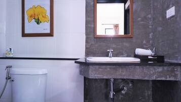 Un baño con inodoro, lavabo y ducha. Hay un cuadro con flores en la pared y un espejo sobre el lavabo.