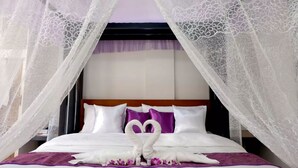 A hotel room with a bed covered in white linens, purple pillows, and a canopy with white lace. - The Tavern Villas at  Orchid Gardens (Bacolor)