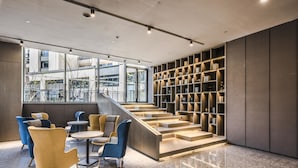 A modern interior with a staircase leading to a mezzanine, featuring a bookshelf and seating area with tables and chairs. - Q-Box Hotel Shanghai Sanjiagang (Shanghai)