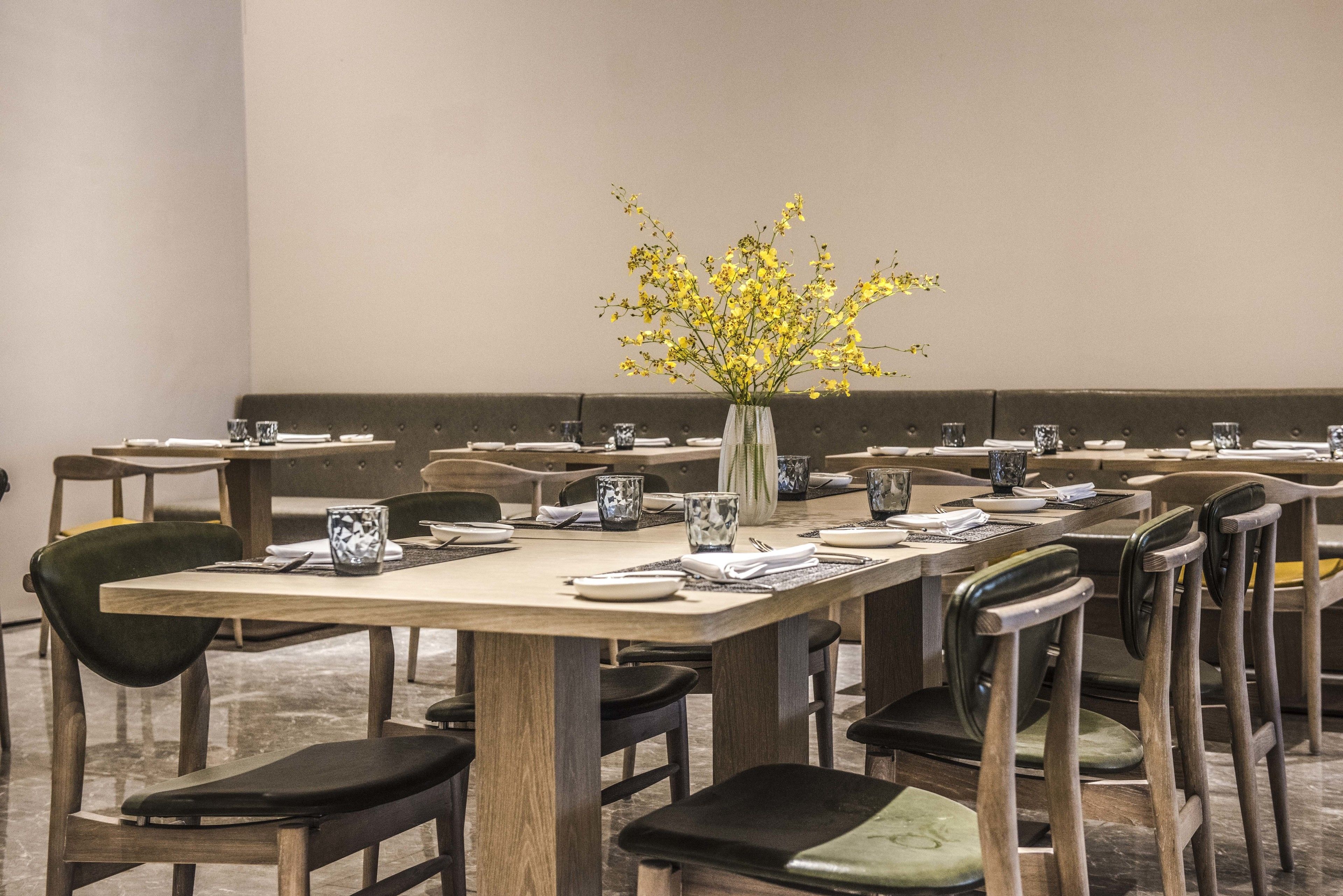 A dining area with multiple tables and chairs, each set with plates, cutlery, and a vase with yellow flowers.