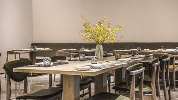 A dining area with multiple tables and chairs, each set with plates, cutlery, and a vase with yellow flowers.