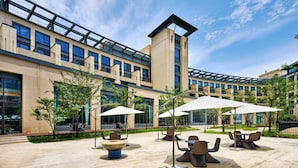 A modern building with multiple floors, outdoor seating areas with umbrellas, and a clear sky. - Q-Box Hotel Shanghai Sanjiagang (Shanghai)