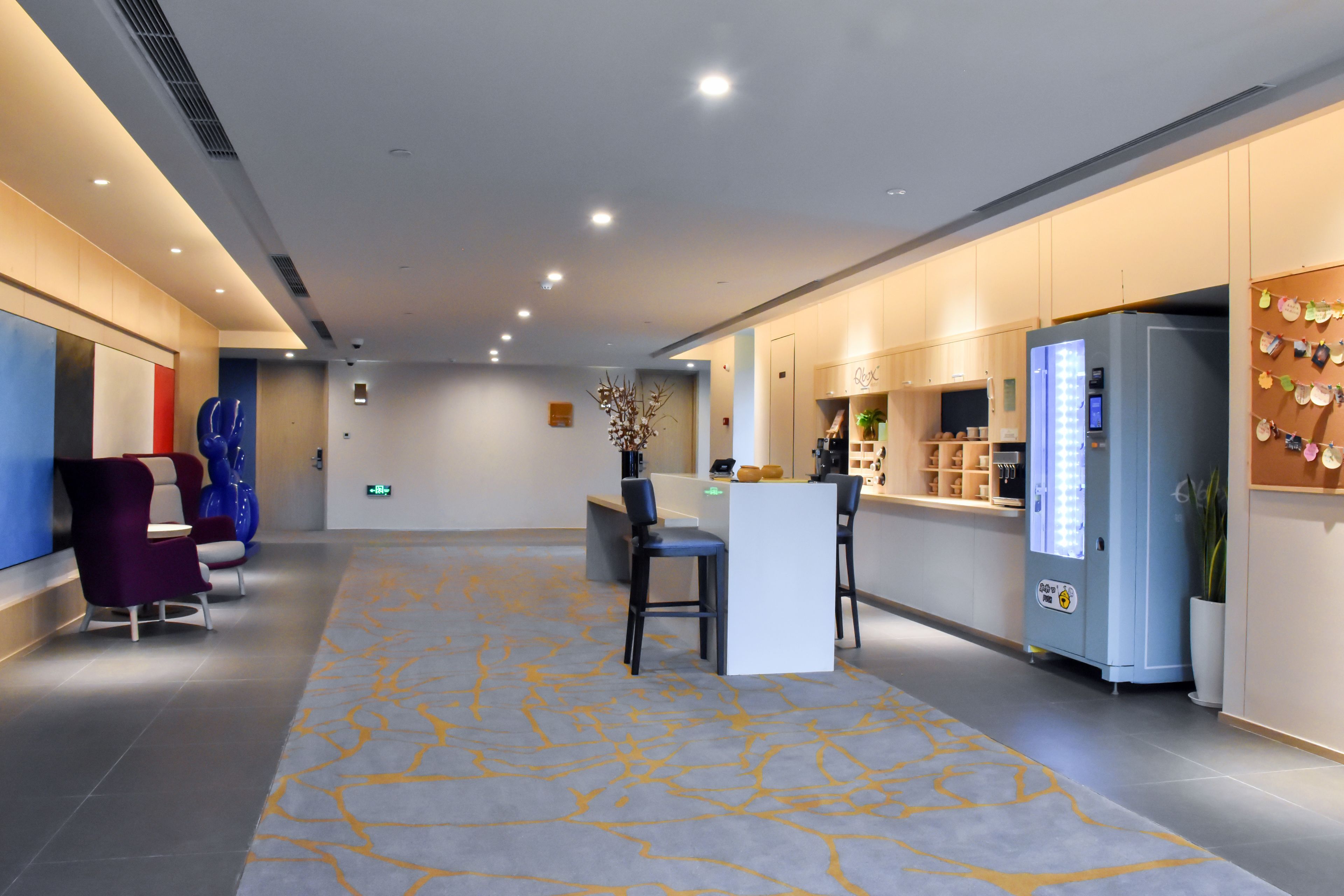 Eine moderne Hotelhalle mit Empfangstresen, Sitzgelegenheiten und einem Automaten.