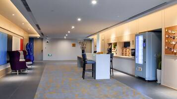 Eine moderne Hotelhalle mit Empfangstresen, Sitzgelegenheiten und einem Automaten.