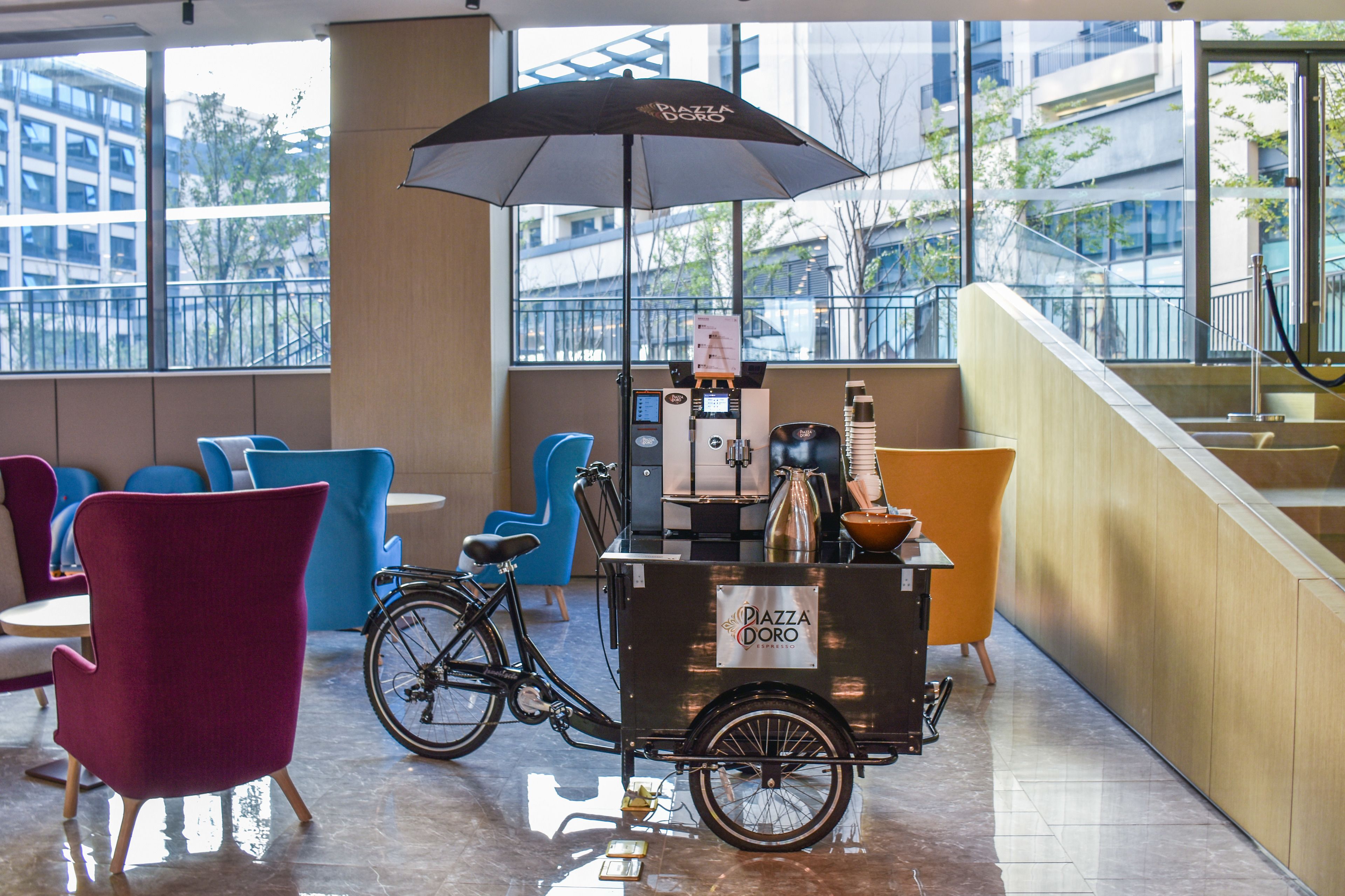 A modern indoor seating area with a coffee cart labeled "Piazza D'oro Espresso" and a bicycle.