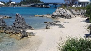 A beach with clear turquoise water, a rocky shoreline, and a bridge in the background. - Stunning sunsets, turtle watching, longtails wheeling and glow worms .... (Somerset Village)