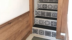 En trappa med mönstrade kakelplattor, trästeg och en inramad tavla på väggen.