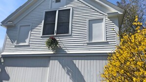 Ett vitt hus med ett takfönster, en liten veranda och ett fönster med en hängande blomkruka.