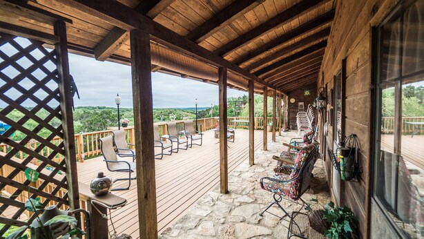 A covered outdoor deck with stone flooring, wooden railings, and multiple seating areas.