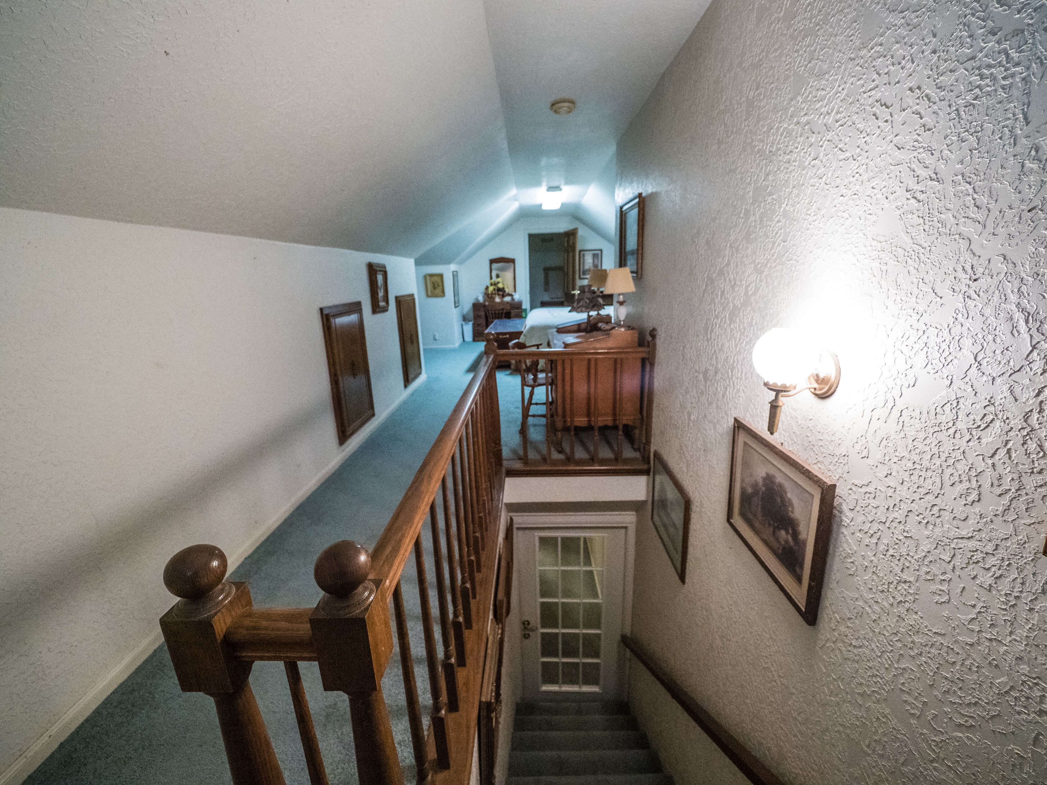 Un escalier étroit avec des rampes et une main courante en bois, menant à un palier où se trouvent une table et des chaises en bois.