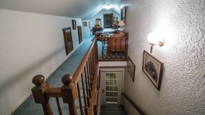 A narrow staircase with wooden railings and a handrail, leading to a landing with a wooden table and chairs.