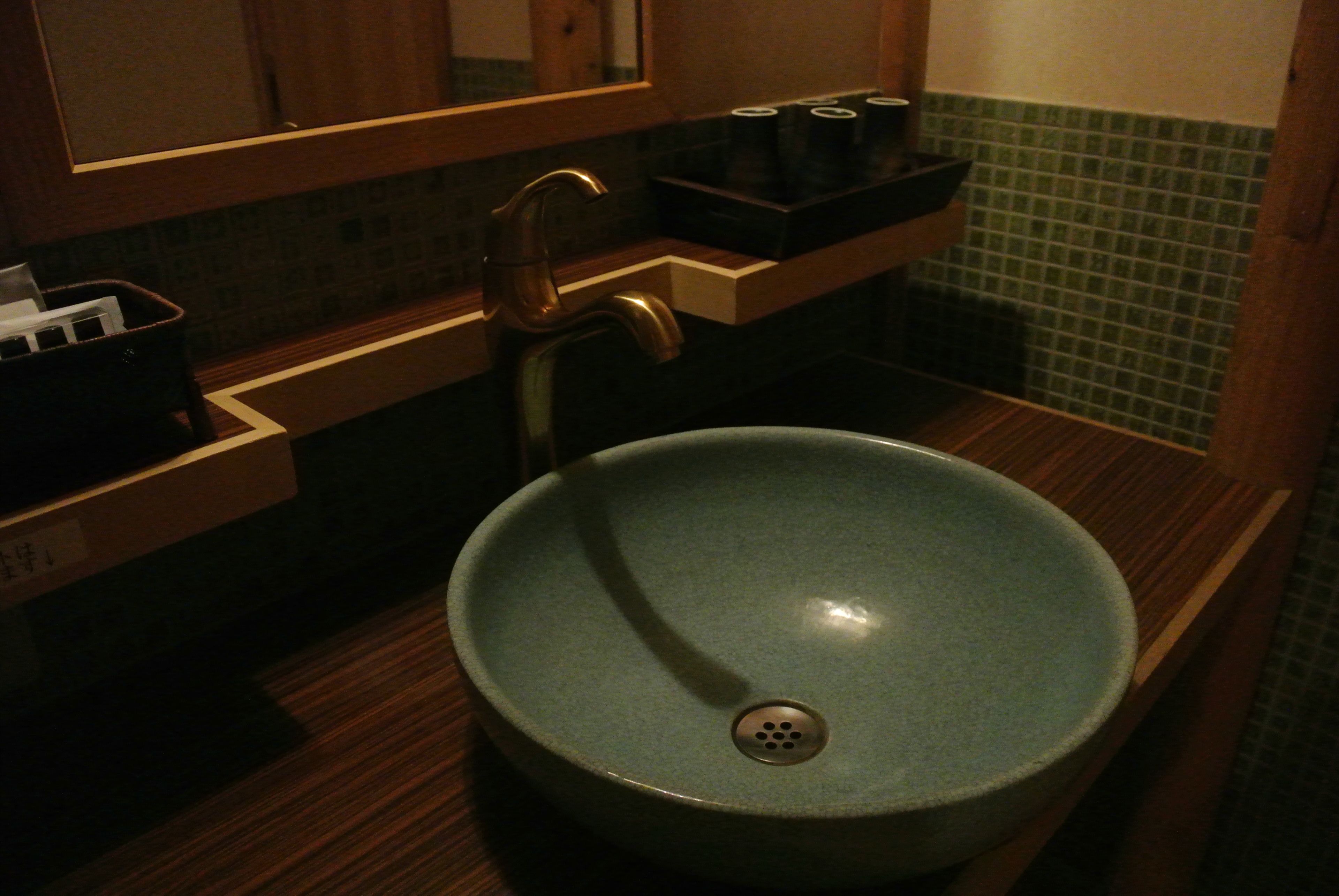 A bathroom with a round, blue ceramic sink, a wooden countertop, a mirror above the sink, and a green tiled backsplash.