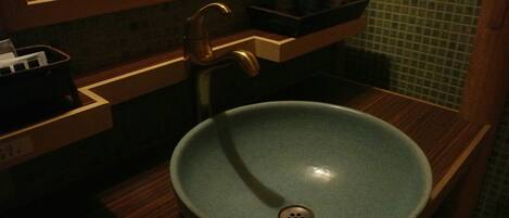 A bathroom with a round, blue ceramic sink, a wooden countertop, a mirror above the sink, and a green tiled backsplash.