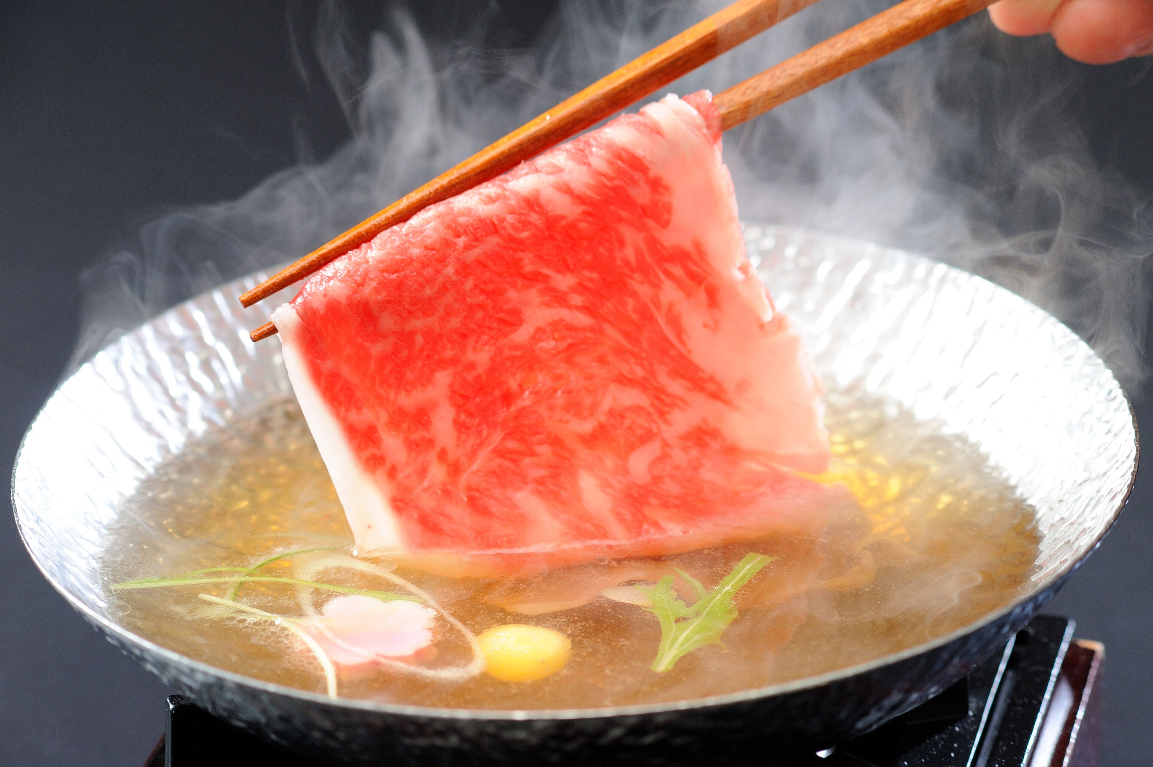 A close-up of a hot pot with a piece of meat being lifted with chopsticks.