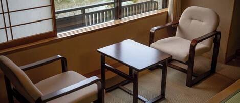 A traditional Japanese room with tatami flooring, a low wooden table, two tatami chairs, and a sliding shoji screen.