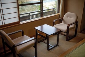 Une pièce de style japonais traditionnel, avec un sol recouvert de tatamis, une petite table en bois, deux chaises en tatami et un paravent coulissant de type shoji.