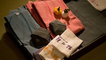 Prendas de ropa ordenadamente dobladas, incluyendo una camisa gris estampada, una camisa roja y una camisa marrón, junto con una toalla blanca con escritura japonesa.
