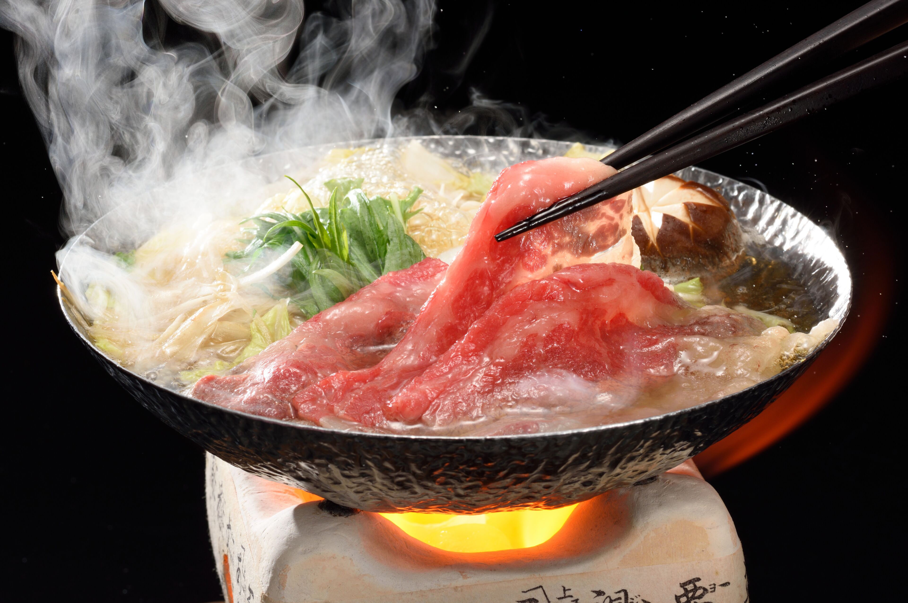 Un cuenco de olla caliente con diversos ingredientes y vapor ascendente.