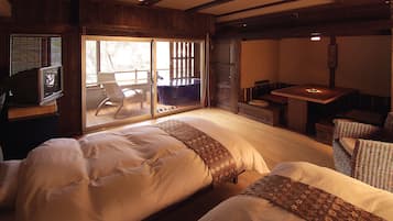 A hotel room with two beds, a small table, and a seating area with a view of the outdoors.