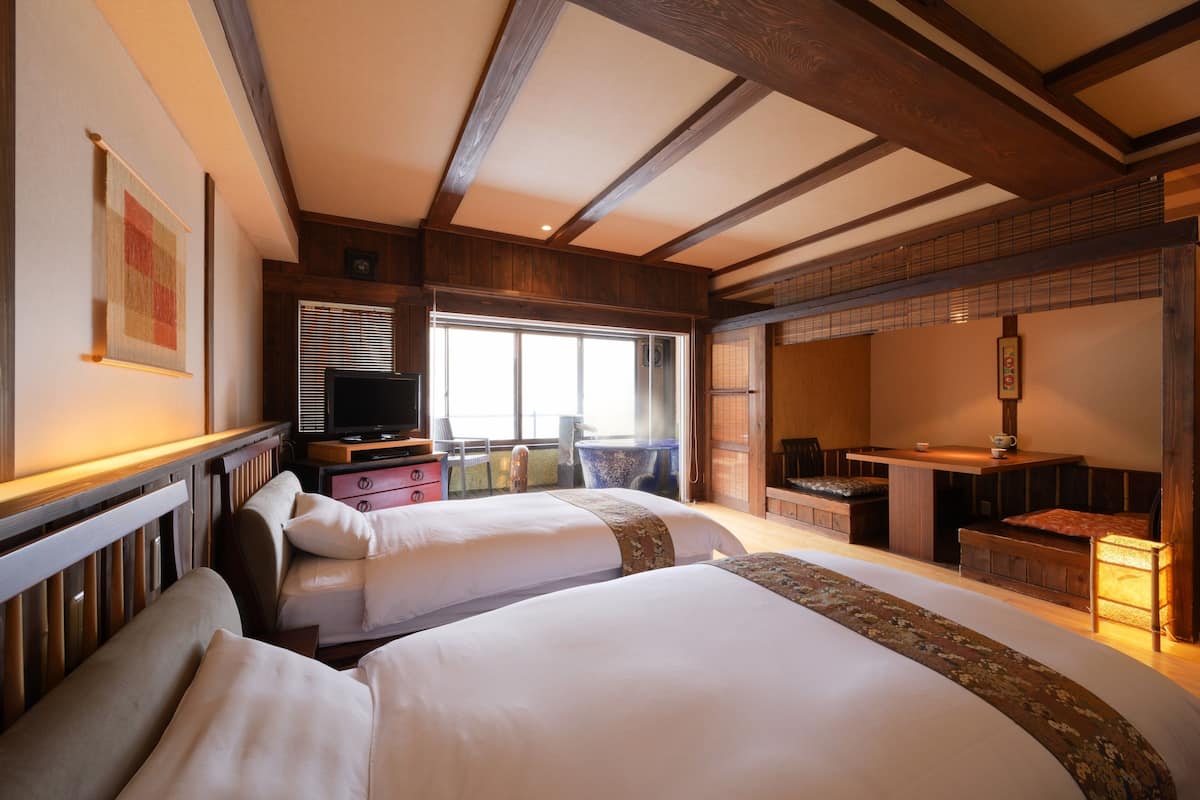 Een hotelkamer met twee bedden, een televisie, een eethoek en een groot raam.