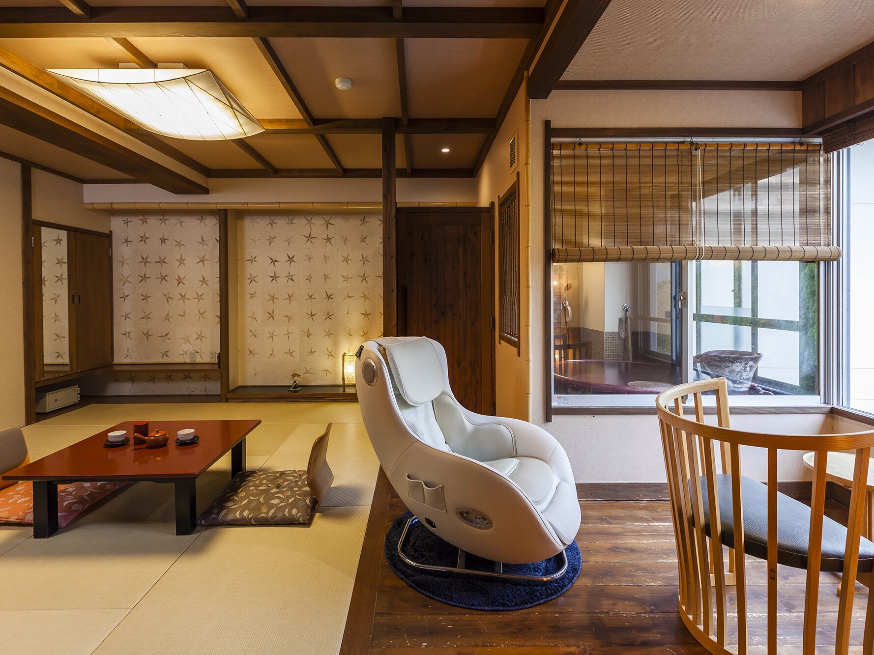 A traditional Japanese room with tatami flooring, a low table, a white cushioned chair, and a wooden table with chairs.