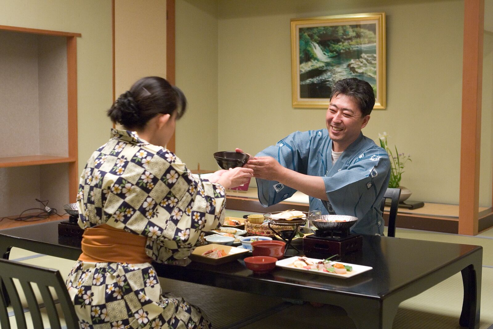 A dining table with various dishes, a painting on the wall, and a traditional Japanese setting.