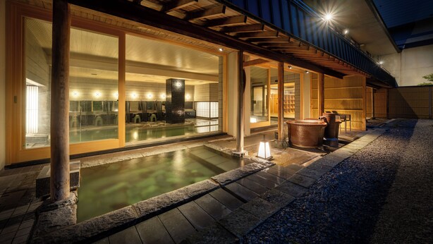 Een traditioneel Japans onsen met een houten terras en een pad van stenen dat naar een warmwaterbron leidt.
