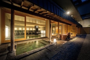 A traditional Japanese onsen with a wooden deck and stone pathway leading to a hot spring.