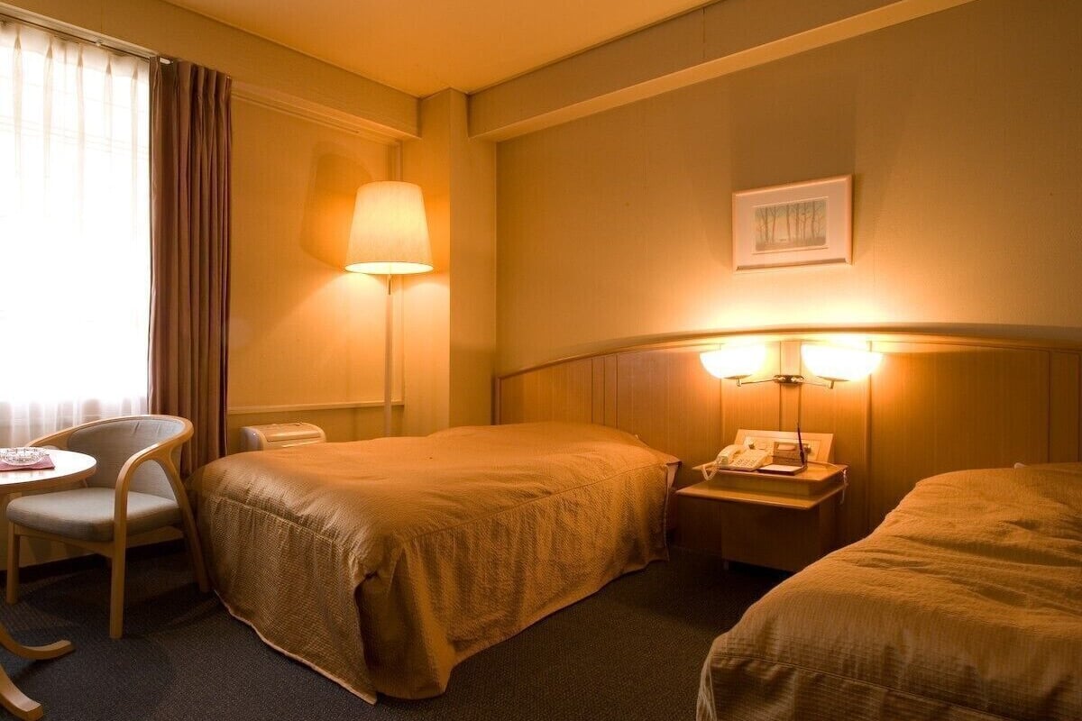 Een hotelkamer met twee bedden, een bureau, een stoel en een nachtkastje met een lamp.