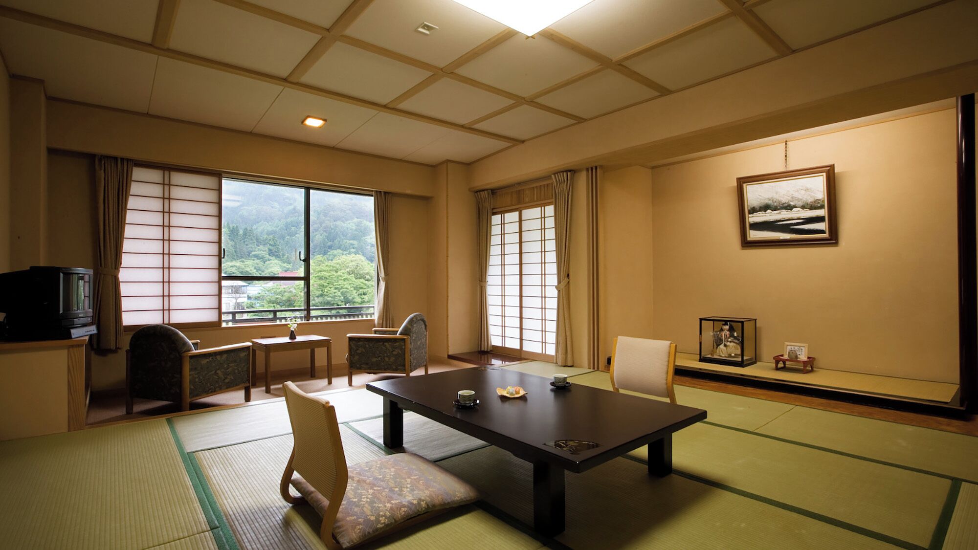 Une pièce de style japonais traditionnel, avec un sol recouvert de tatamis, une table basse, des chaises, un téléviseur et un tableau encadré accroché au mur.