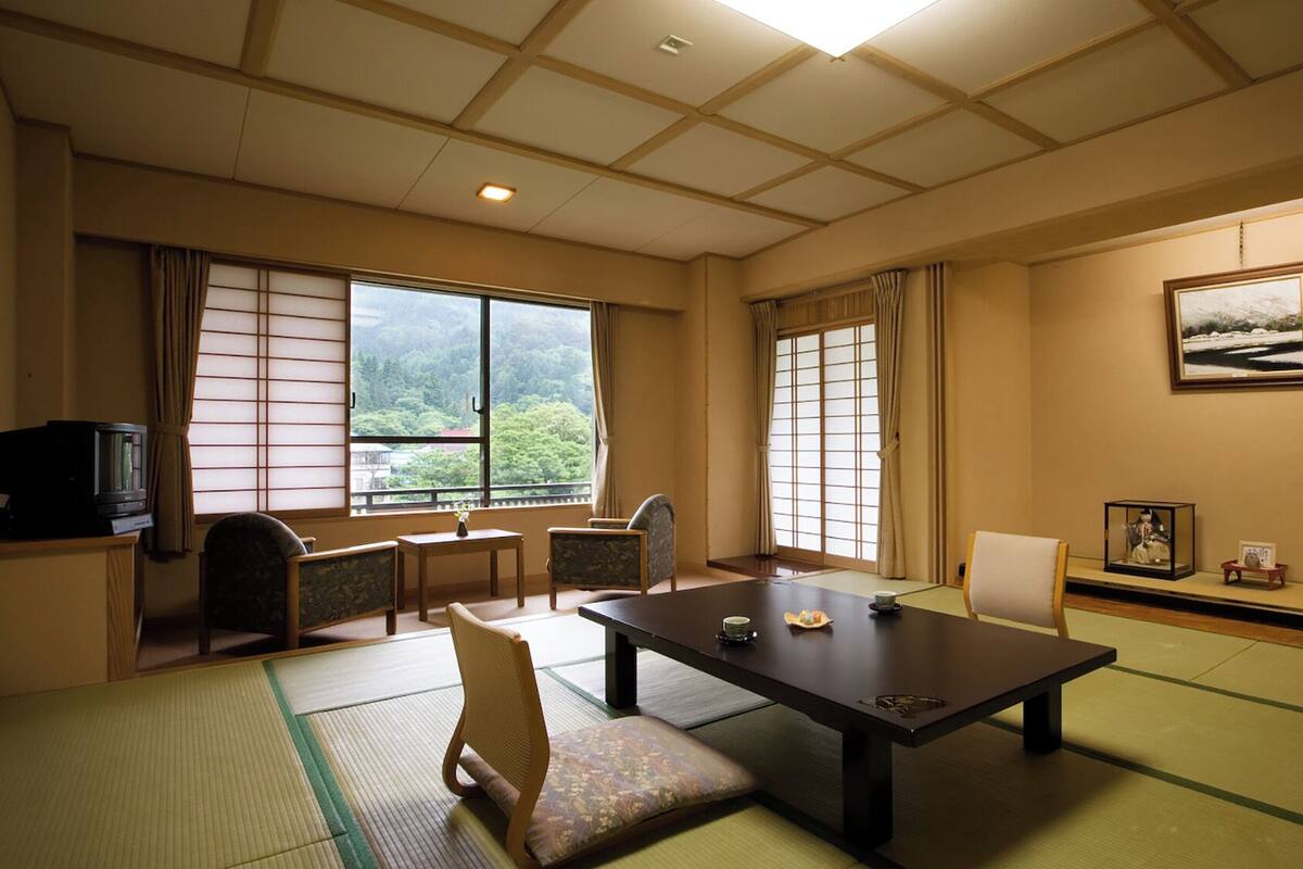 Een traditionele Japanse kamer met tatami vloerbedekking, een lage tafel, stoelen, een televisie en een ingelijst beeld aan de muur.