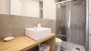 Ein modernes Badezimmer mit einem weißen Waschbecken, einer Holzabdeckung und einer Duschkabine aus Glas.