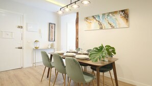 Ein Essbereich mit einem Holztisch, gedeckt für vier Personen, umgeben von grünen Stühlen, einer großen Pflanze und einem Gemälde an der Wand.