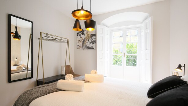 Ein Schlafzimmer mit einem großen Bett, einem Spiegel, einer Pendelleuchte und Blick auf Grünfläche.