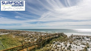 Ein Küsteneigentum mit einer Holzpromenade, die zum Strand führt, umgeben von Dünen und Vegetation.