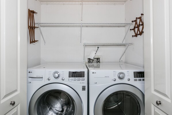 Ein Waschraum mit zwei weißen Waschmaschinen mit Frontlader, einem Wäscheständer aus Metall und Holztrocknern an der Wand.