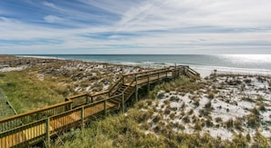 Ein Küsteneigentum mit einer Holzpromenade, die zum Strand führt, umgeben von Dünen und Vegetation.