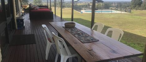Una terrassa de fusta amb taula i cadires, un sofà vermell, i vista a una piscina i un paisatge.