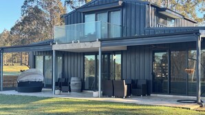 Une maison moderne à deux étages, dotée d’un patio couvert, de grandes fenêtres et d’un espace salon extérieur.