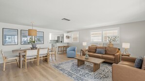 Ein geräumiges Wohnzimmer mit einem Holzespeisetisch, blauen Stühlen, einem blauen Sessel, einem braunen Sofa und einem Couchtisch.