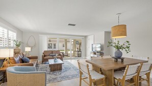Ein geräumiges Wohnzimmer mit einem Holzessttisch, Korbstühlen, einem braunen Ledersofa und einem großen Fenster.
