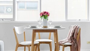 A dining table with white chairs, a vase with flowers, and a window with a view of buildings. - Bright & Sunny Oasis (Balaclava)