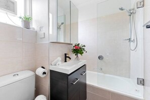 A modern bathroom with a toilet, sink, mirror, and shower. - Bright & Sunny Oasis (Balaclava)