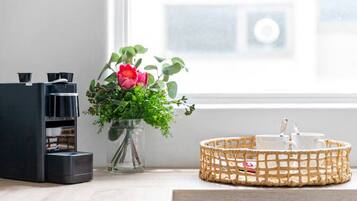 A coffee machine, a vase with a flower, and a basket with cups on a wooden surface.
