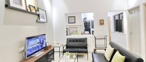 A living room with a flat-screen TV, a sofa, a coffee table, and a bookshelf.