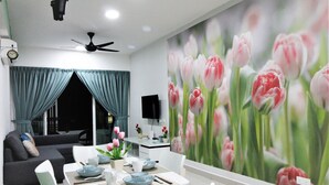 A modern living room with a dining area, featuring a sofa, a TV, and a wall with a floral mural. - H2H Holland Cottage (Ipoh)
