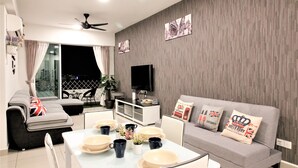 A modern living room with a grey sofa, a dining table with plates and cups, a flat-screen TV, and a ceiling fan.