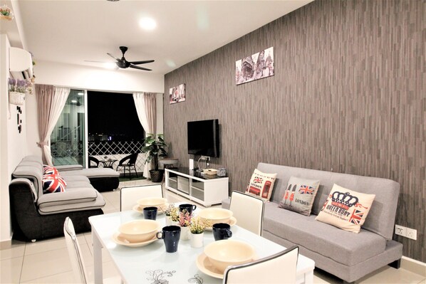 Una sala de estar moderna con un sofá gris, una mesa de comedor con platos y tazas, un televisor de pantalla plana y un ventilador de techo.